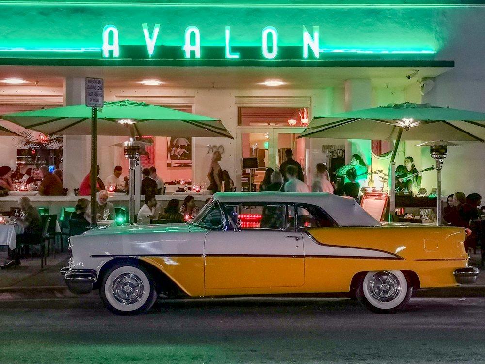 Vintage yellow convertible parked outside a neon Ocean Drive restaurant